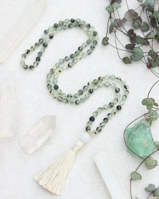crystal mala made with prehnite beads and white jade with a cream tassel, surrounded my white crystals and leaves